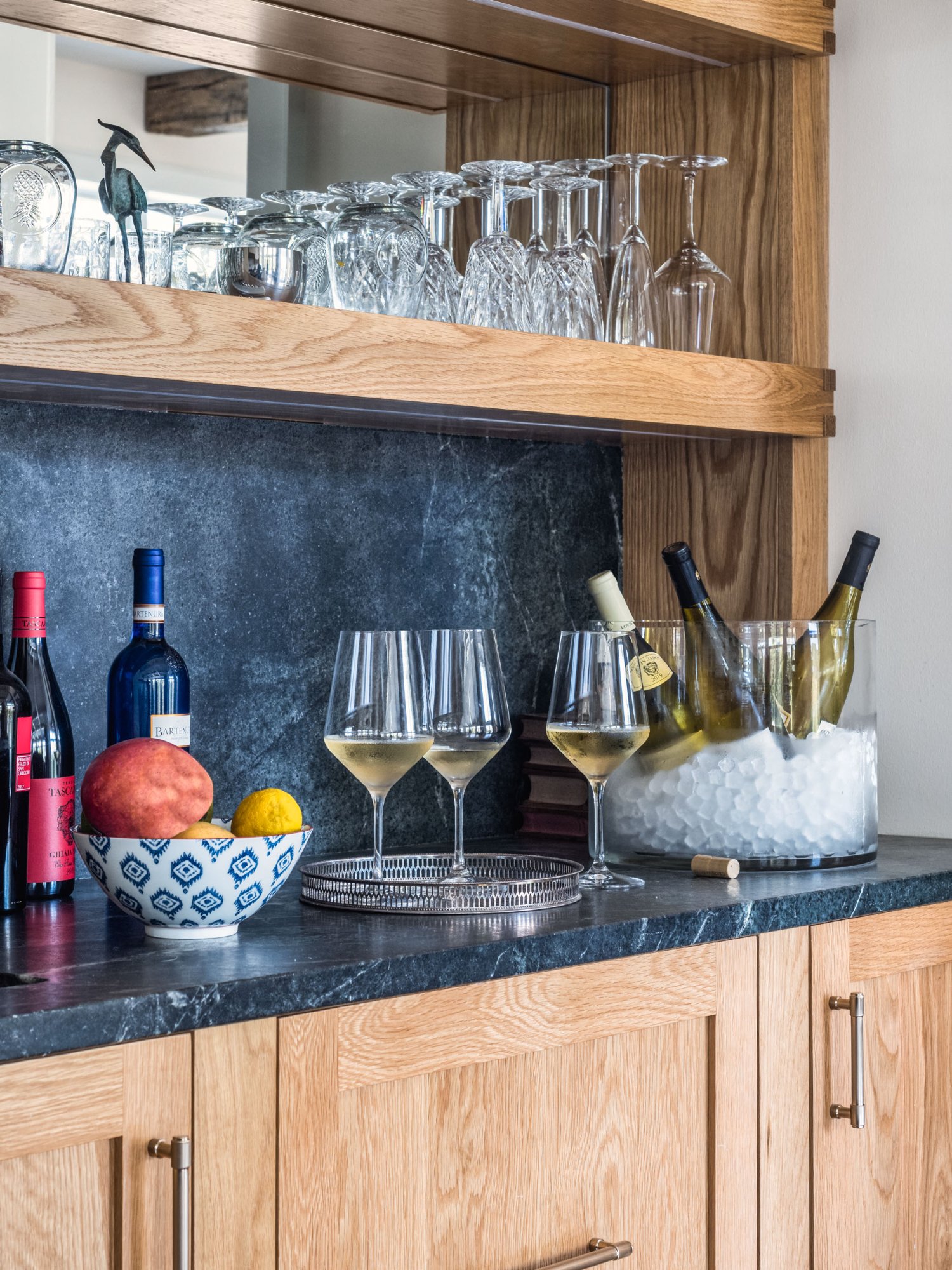 Bar detail showing soapstone counter with crystal stemware on oak shelves, wine glasses, and styled accessories — Nordic Farmhouse