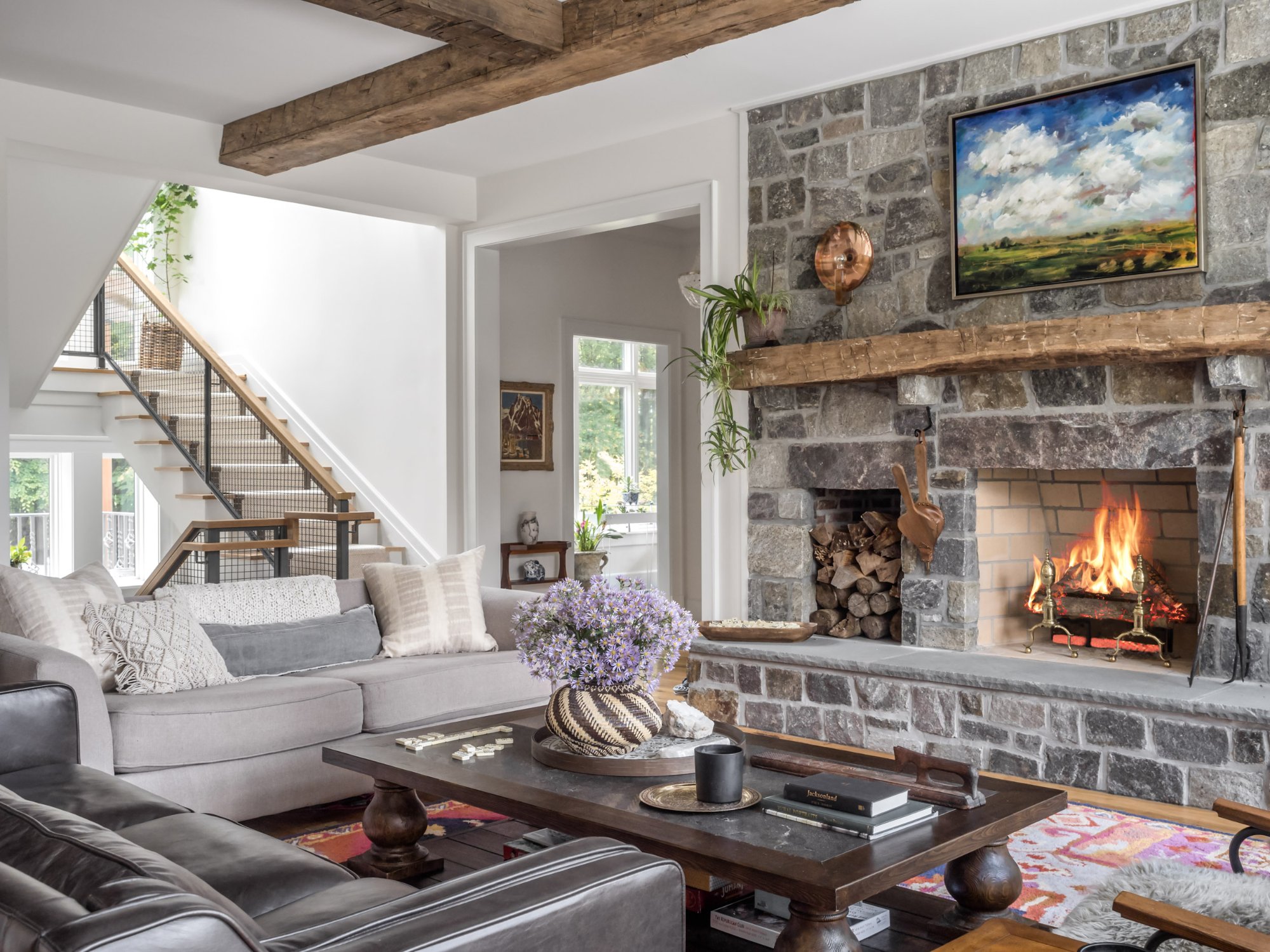 Great room from fireplace side showing staircase, reclaimed beams, leather seating, and landscape painting — Nordic Farmhouse