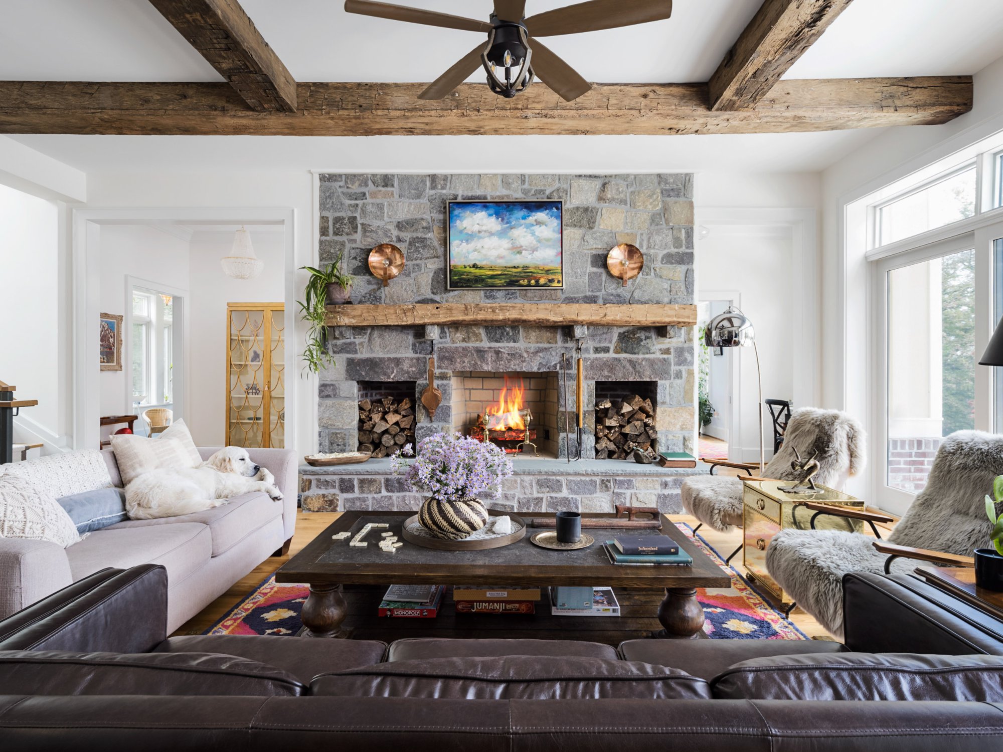 Great room with full-height stone fireplace, reclaimed timber beam ceiling, leather and linen seating, sheepskin throws, and colorful rug — Nordic Farmhouse