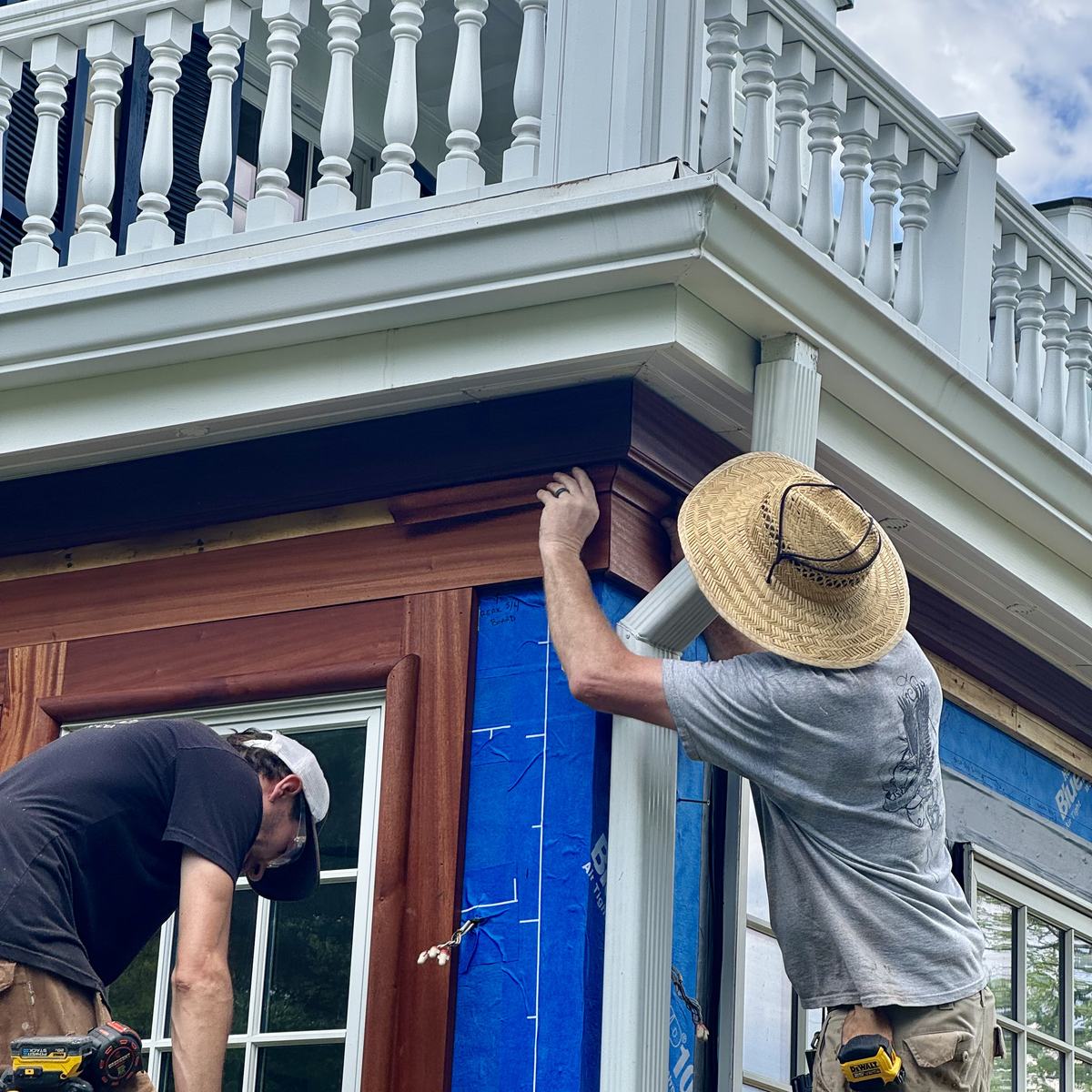 Carpenters hand-fitting sapele trim at the porch cornice beneath the original balustrade — North Winds Porch, Towson