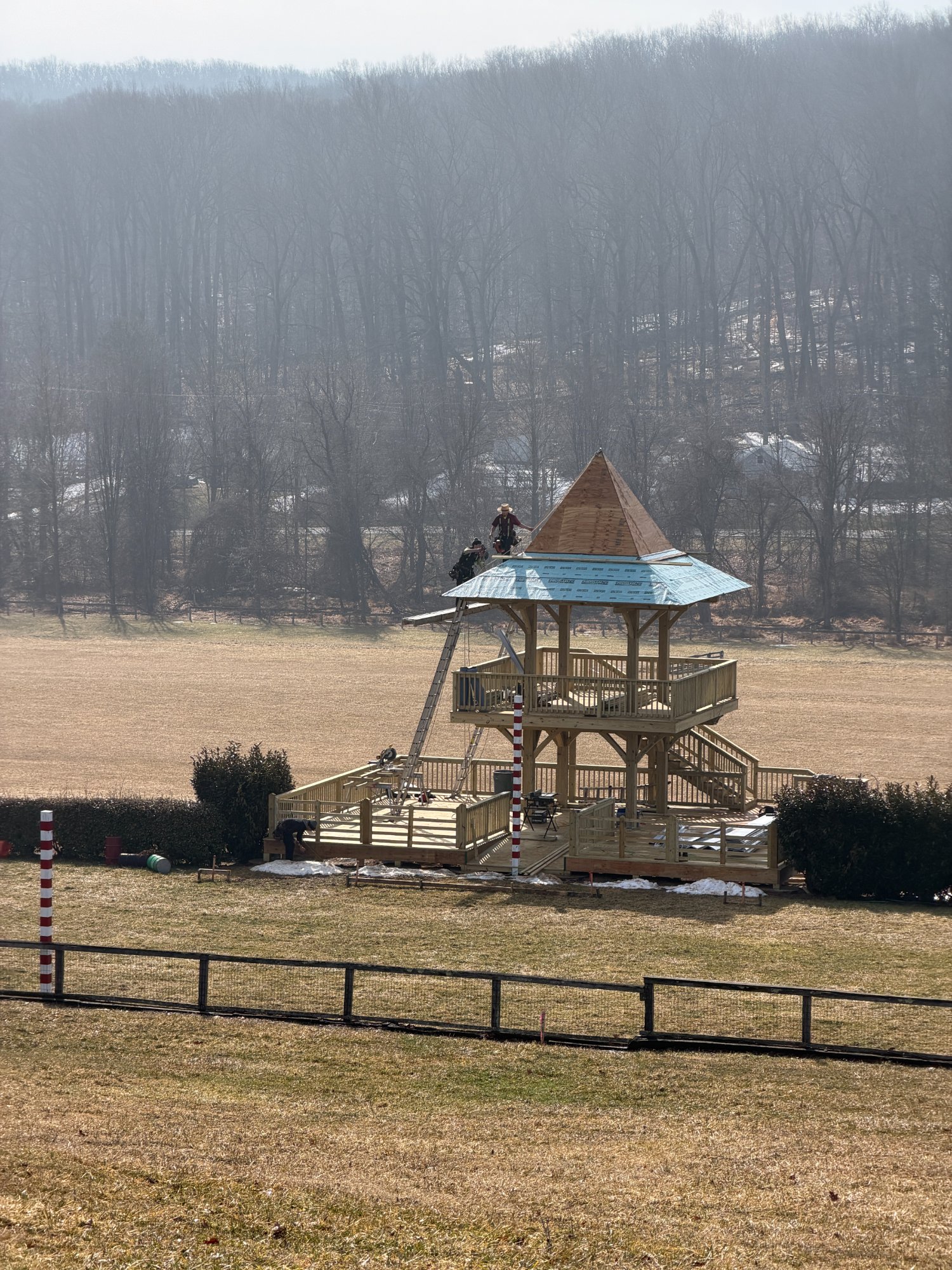 New tower under construction with timber frame complete, crew installing roof sheathing, winter countryside beyond — Shawan Downs