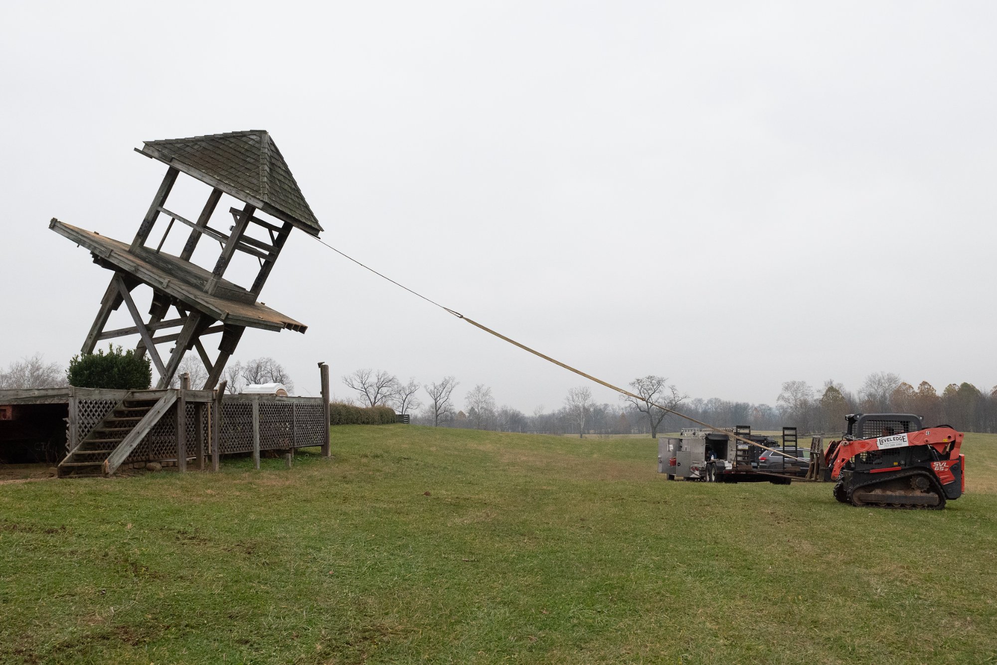 Skid steer pulling the old tower with cable, structure leaning and beginning to give way — Shawan Downs demolition