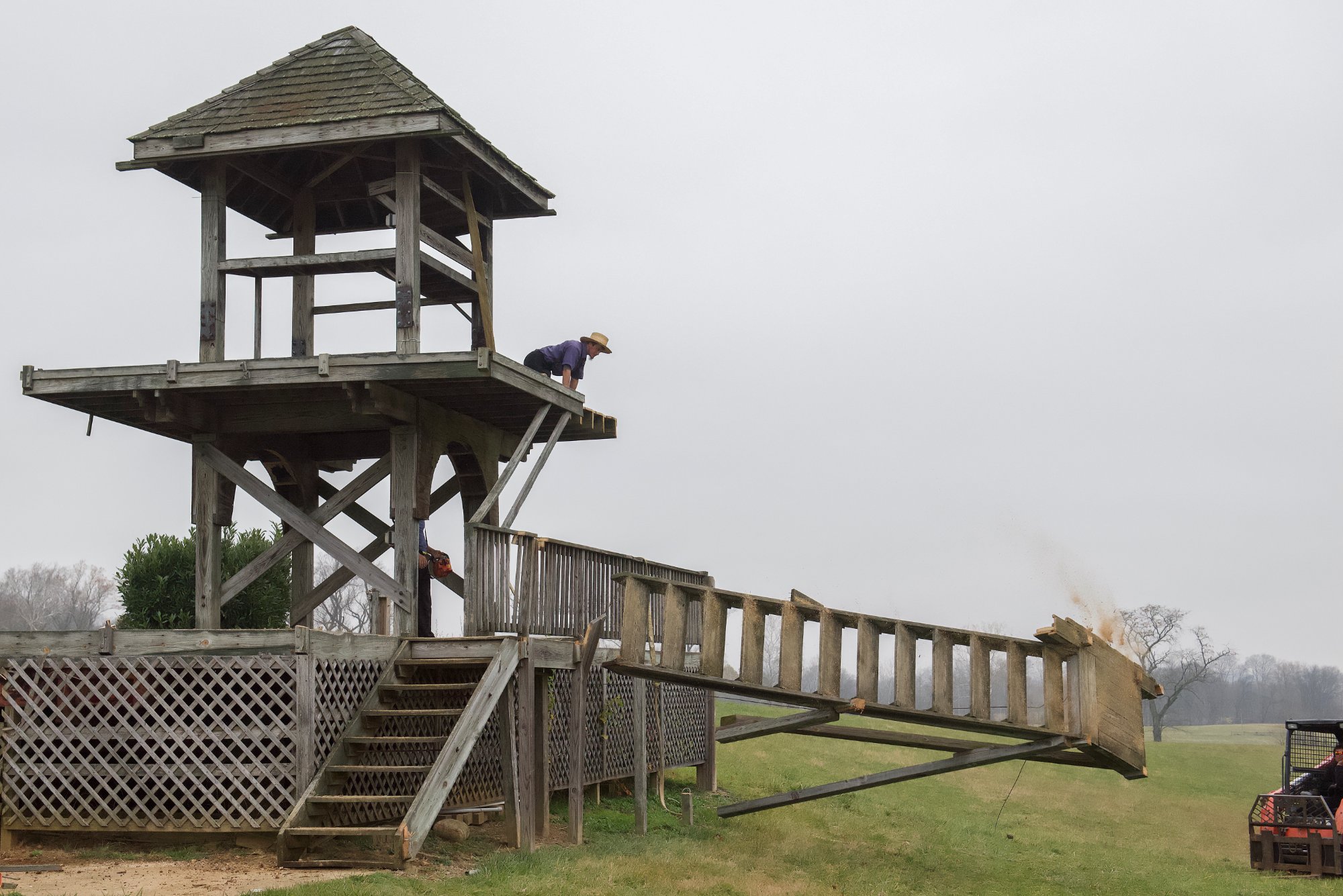 Chainsaw operator cutting the staircase free as the railing section falls away from the tower — Shawan Downs demolition